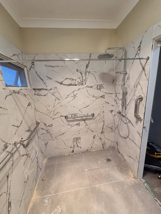 Accessible Shower Fit-Out: marble-tiled shower with grab rails and rain shower head